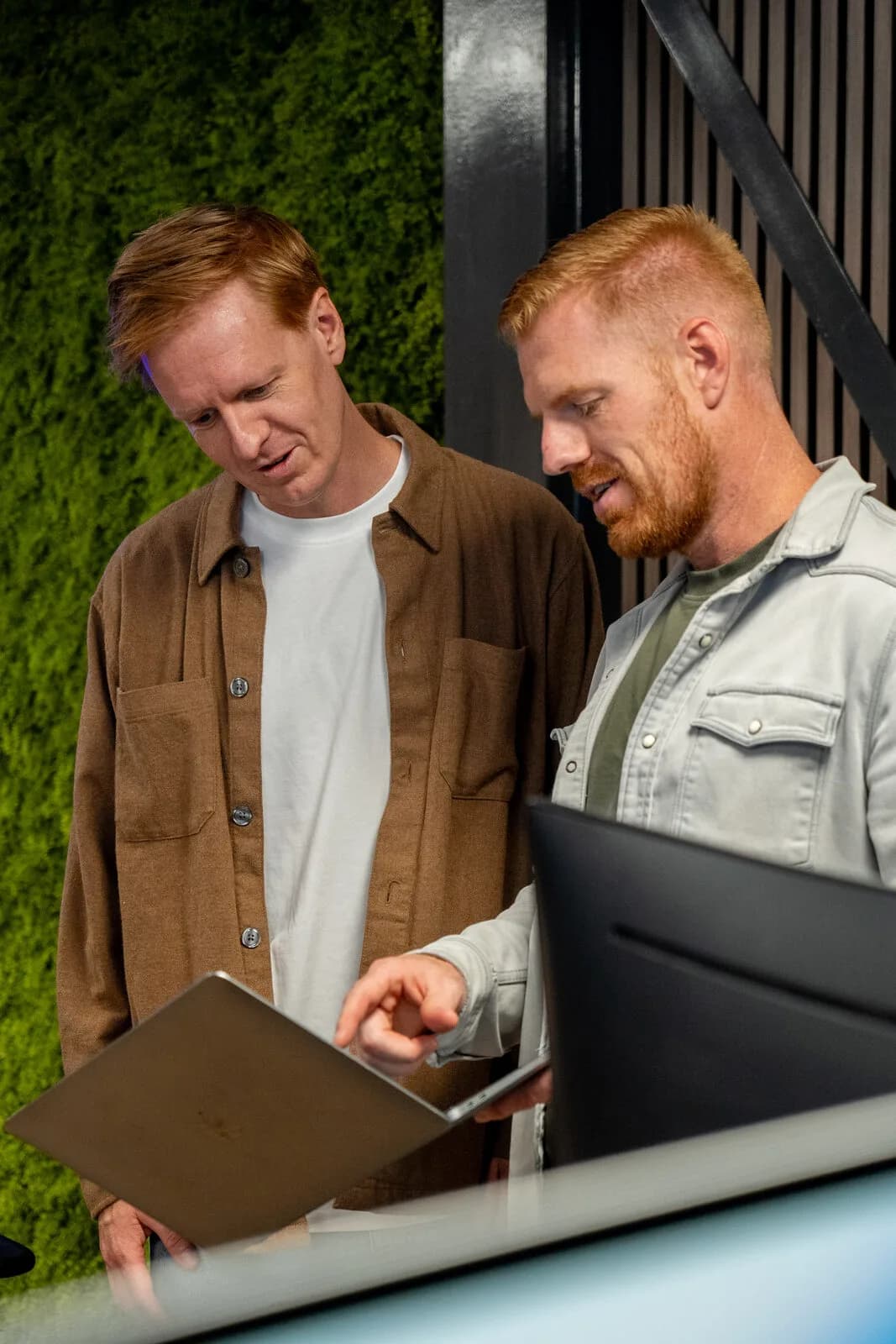 Twee collega's van Acclerate kijken samen naar een laptop bij de groene wand