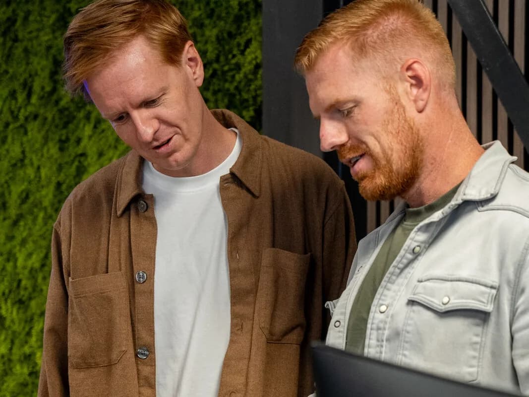 Twee collega's van Acclerate overleggen samen bij de groene wand op kantoor